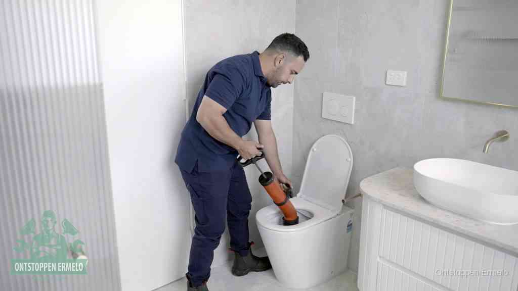 Een monteur buigt over een wandcloset en duwt met de hand een persluchtontstopper in de toiletpot om de verstopping handmatig los te maken in Ermelo