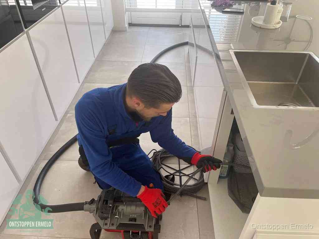 Een monteur ontstopt de keukenafvoer onder de spoelbak met een elektrische veermachine in Ermelo