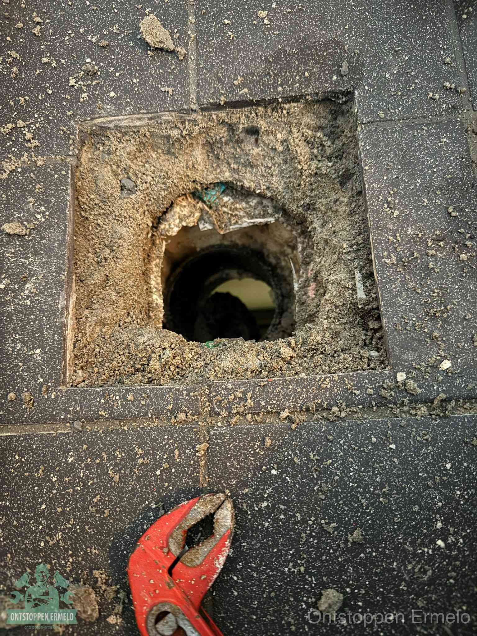 Een geopend rioolputje in een betontegelvloer met losgemaakt rooster en een zichtbare ronde afvoerbuis, het achterhalen waar de afvoerverstopping zit in Ermelo