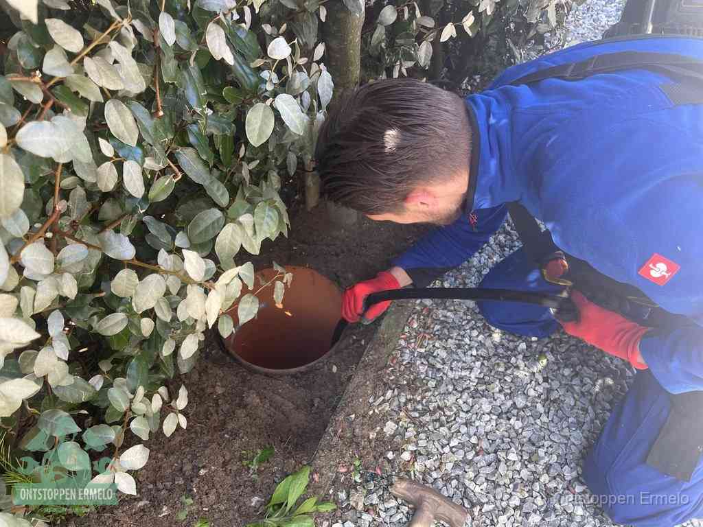 Een monteur voert een slang in een geopende rioolput in de tuin om het hoofdriool te ontstoppen in Ermelo
