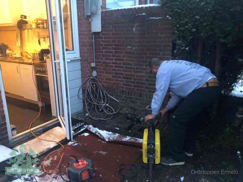 Een monteur werkt buiten bij een open riool-/grondput met een elektrische ontstoppingsmachine om een verborgen afvoerprobleem op te sporen in Ermelo