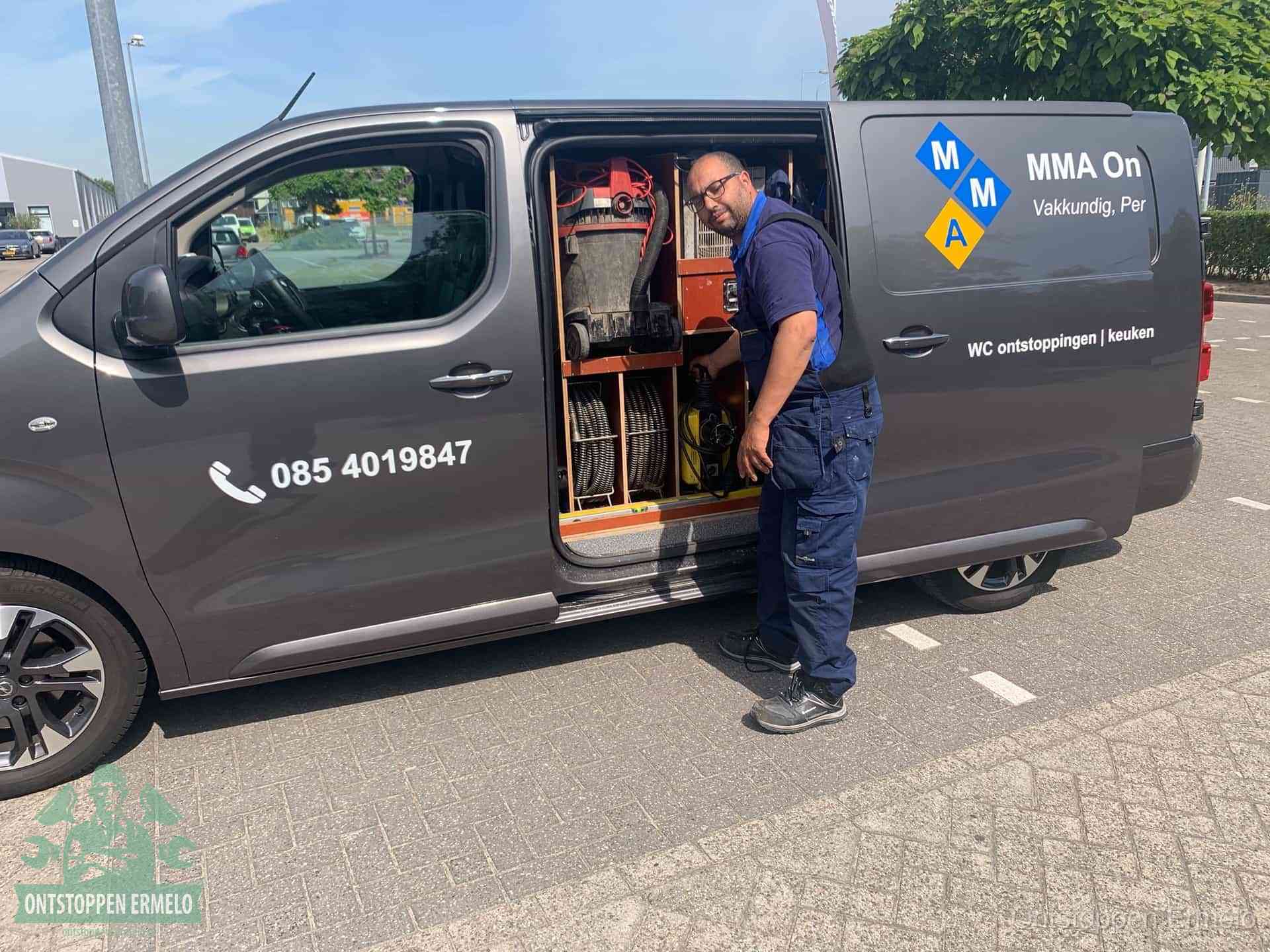 Een monteur bij de open schuifdeur van zijn bedrijfsbus op een parkeerplaats, klaar om de oorzaak van terugkerende afvoerverstoppingen aan te pakken in Ermelo