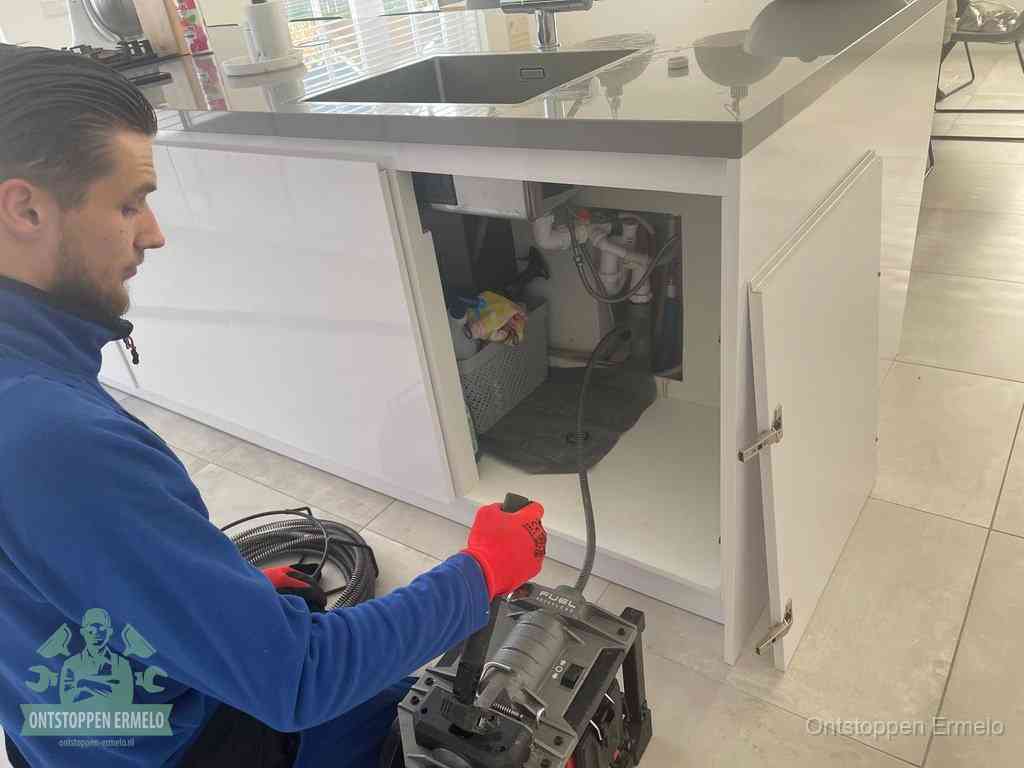 Monteur ontstopt met een veermachine een verstopte afvoer onder de gootsteen in Ermelo