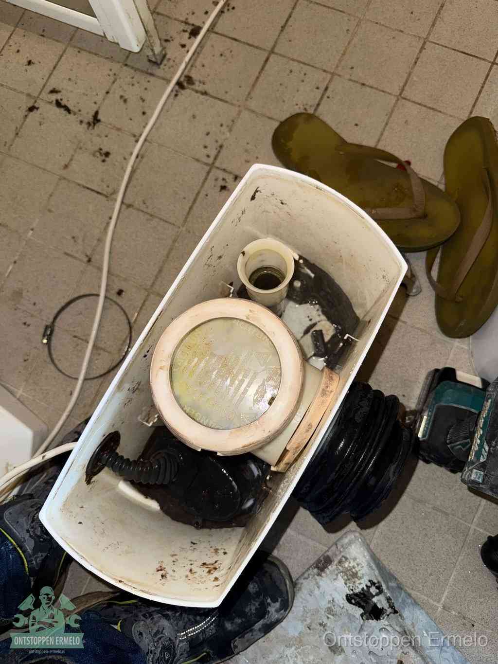 Een gedemonteerde toiletpot op de vloer met ontstoppingsveer en gereedschap ernaast, het verwijderen van een vastzittend voorwerp uit de wc in Ermelo