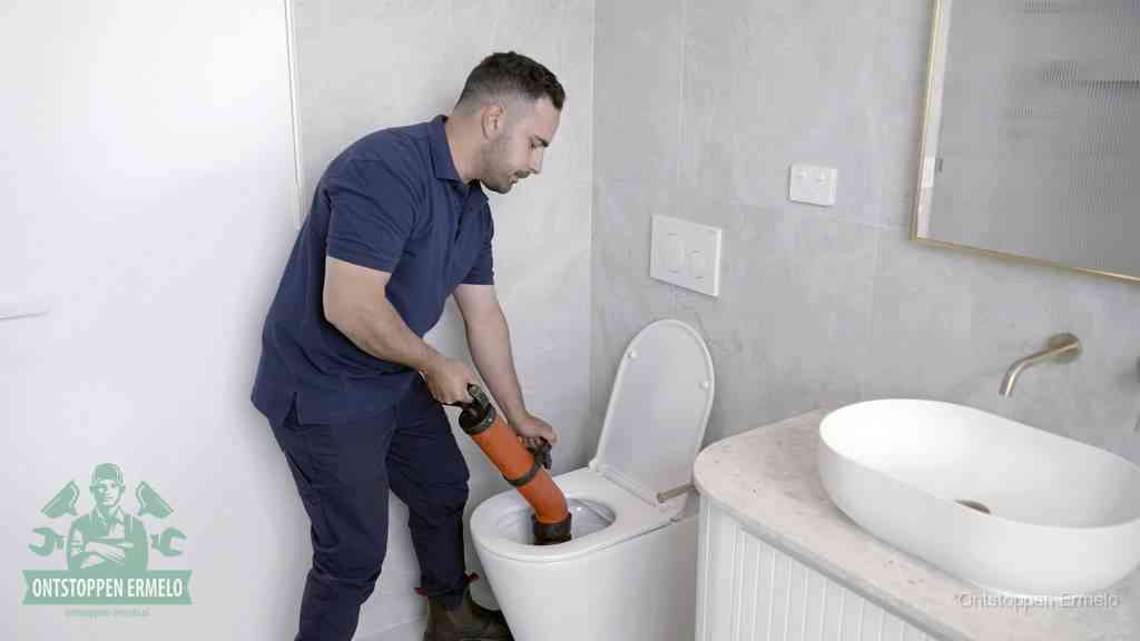 Een man gebruikt een handmatige luchtdruk-ontstopper in een modern betegeld toilet om zelf de wc te ontstoppen in Ermelo